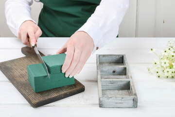 Florist at work: woman shows how to make Easter floral table decoration with arabian star flowers and gypsophila paniculata twigs in simple wooden box. Step by step, tutorial.