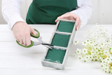 Florist at work: woman shows how to make Easter floral table decoration with arabian star flowers and gypsophila paniculata twigs in simple wooden box. Step by step, tutorial.