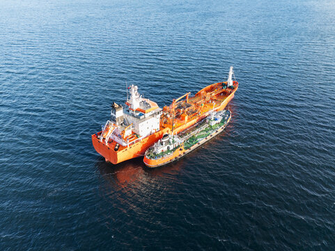 Aerial drone view of a bunker vessel refueling a large industrial tanker ship in the open waters of Baltic Sea.