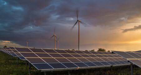A solar farm near a wind farm against a dynamic sky