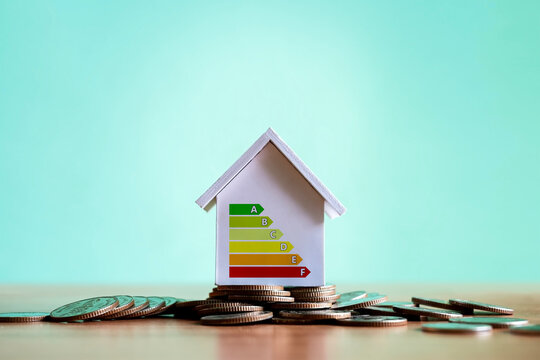A model house with an energy efficiency meter based on a stack of coins; a concept for saving energy in homes, sustainable real estate investment, and eco-friendly housing.