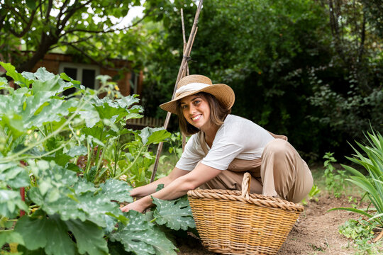 Smiling young woman wearing hat working in vegetable garden during curfew