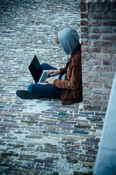 Teenager using laptop and sitting on a stone floor in the city
