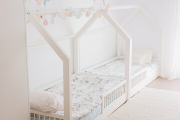 Minimalist kids bedroom with two white house beds, floral bedding and soft pastel garland in bright light.