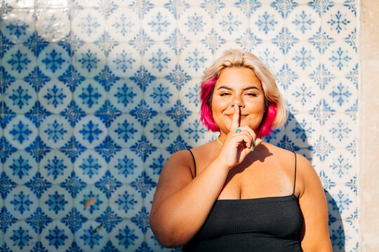 Woman showing silence sign with finger on lips against wall