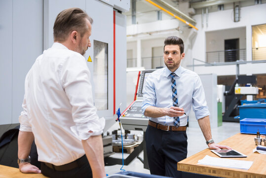 Two businessmen at table in factory shop floor discussing