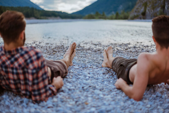 Germany, Bavaria, back view of two friends lying at riverside looking at view