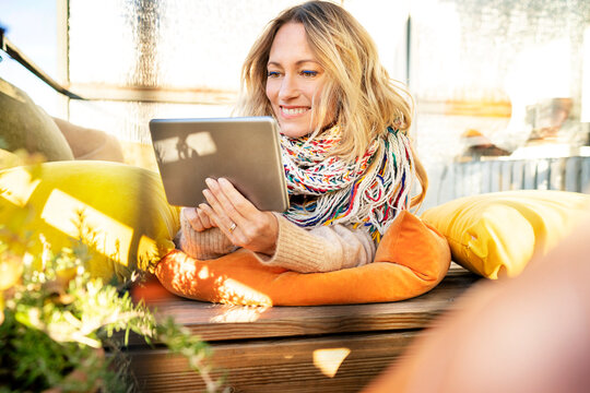 Portrait of smiling blond mature woman relaxing in winter garden using digital tablet