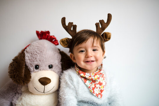 Portrait of happy baby girl with reindeer antlers headband beside her toy dog