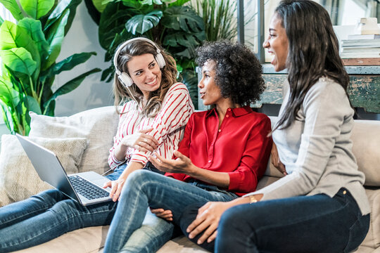 Three happy women with laptop sitting on couch