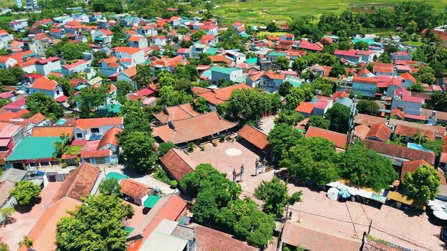 Drone shot over the historic Duong Lam village, showing traditional Vietnamese architecture, red-tiled roofs, and a central communal house square surrounded by lush trees