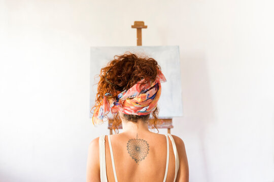 Rear view of young female painter in art studio in front of empty canvas