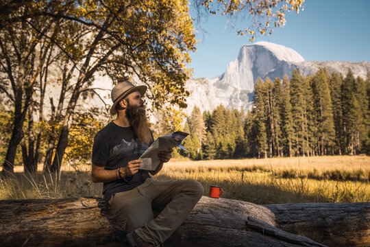 USA, California, bearded man with a map sitting on a log in Yosemite National Park