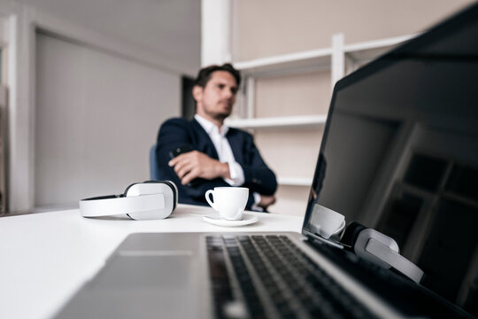 Laptop, headphones, coffee cup and businessman in background