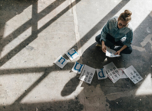 Young woman sitting on concrete floor working on letter templates