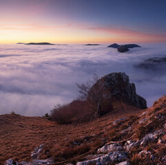 Sunset with clouds, sun rays, and misty valleys witn forest, mountain and peak nature landscape.