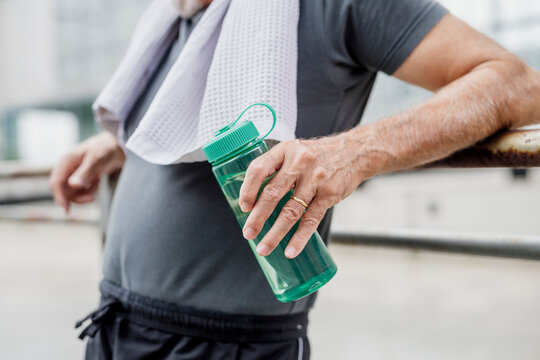 Close-up of senior man holding water bottle while standing in city