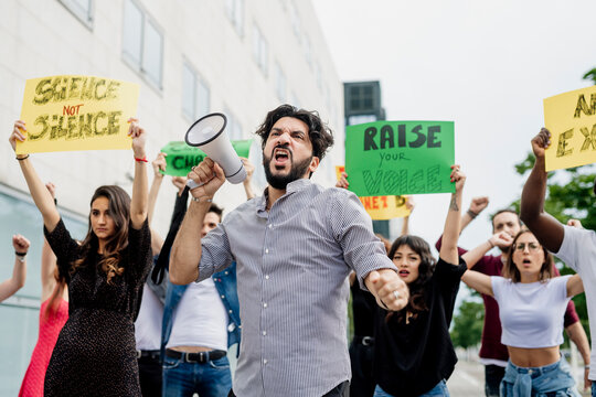 Man screaming through megaphone while protesting with people on street in city
