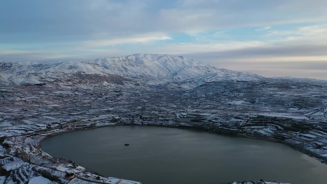 Aerial view of Lake Ram at a winter sunrise in the Golan Heights with the snowy Mount Hermon and Majdal Shams in the background