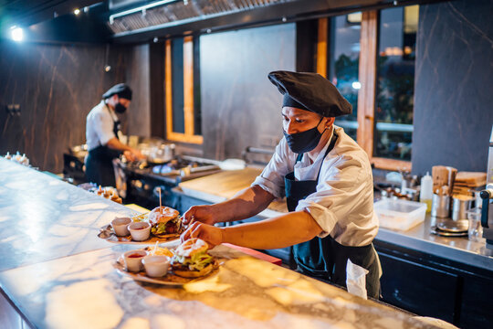Chef wearing protective face mask preparing burgers in restaurant kitchen