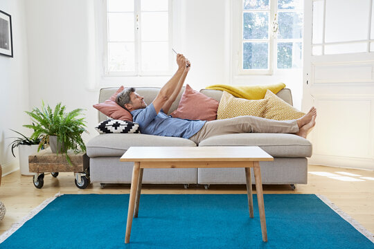 Man lying on couch at home, using digital tablet