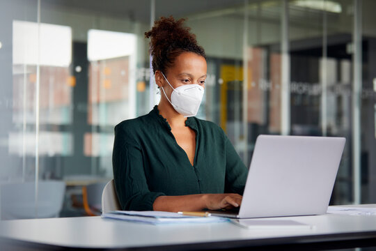 Portrait of businesswoman wearing protective mask working on laptop at counter