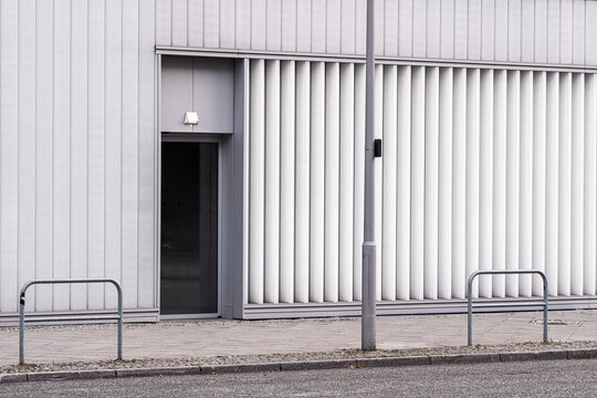 Minimal modern architecture with a metal door entrance set in an urban wall facade creating a clean exterior with simple lines and empty street space