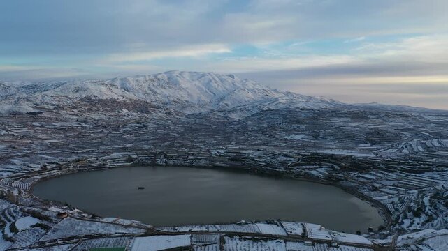 Aerial view of Lake Ram at a winter sunrise in the Golan Heights with the snowy Mount Hermon and Majdal Shams in the background
