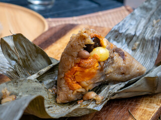 Traditional Thai sticky rice dumpling zongzi wrapped in dried leaves with savory filling on rustic wooden plate