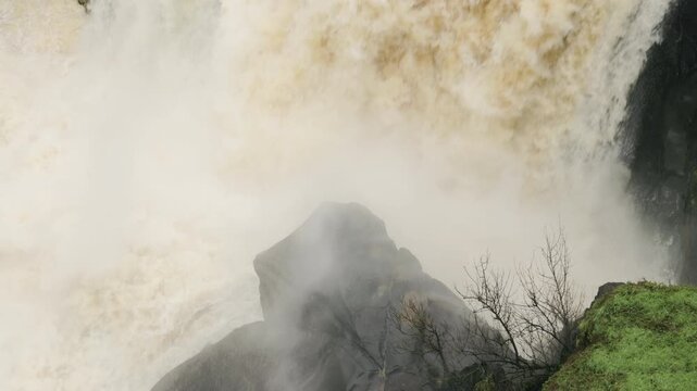 Powerful waterfall gushing muddy water over rugged rocks during a flood, showcasing the raw force and danger of a river in spate, creating a spectacular natural display