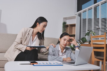 Two businesswomen feeling stressed while working on laptop in office