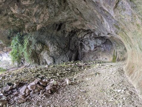 Interno di una grotta con rocce, muschio e luce naturale laterale; atmosfera selvaggia, texture geologiche, natura incontaminata, esplorazione, avventura.