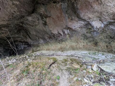 Interno di una grotta con rocce, muschio e luce naturale laterale; atmosfera selvaggia, texture geologiche, natura incontaminata, esplorazione, avventura.