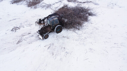 Industrial tractor with hydraulic grapple clearing brush in winter field © Andrey