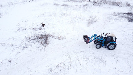 A high-angle drone shot of a modern blue tractor parked or working in a vast, pristine white snow field