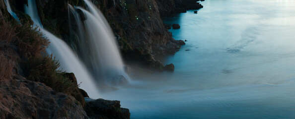 A waterfall cascading from the cliffs into the sea. © daphnusia