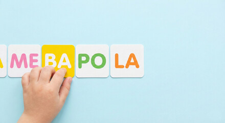 Child's hand arranging colorful syllable cards in a row on blue background, early reading and literacy concept