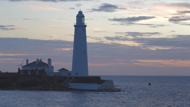 A static medium shot of the historic St Mary&rsquo;s Lighthouse in Whitley Bay during a winter dawn. The white tower and red-roofed cottages sit on a tidal island