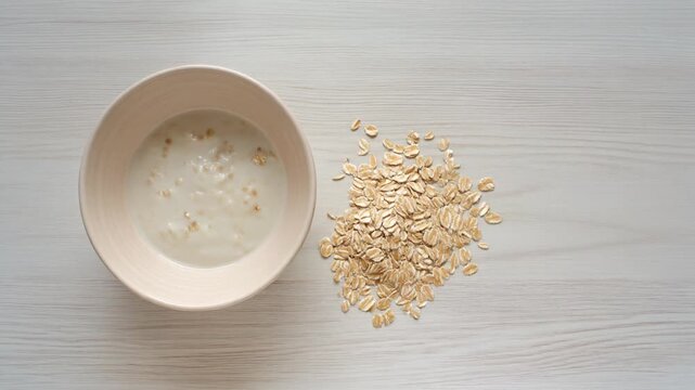 Simple Breakfast Bowl and Spilled Oats. Neo-Minimalism & Quiet Luxury. A simple white matte ceramic bowl containing a few spoonfuls of porridge or yogurt with a small aesthetically pleasing.
