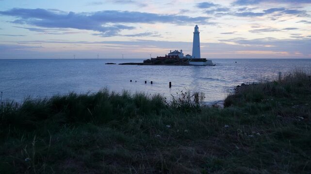 A scenic wide shot of the historic St Mary&rsquo;s Lighthouse on its tidal island in Whitley Bay, captured from low coastal cliffs framed by blowing sea grass.