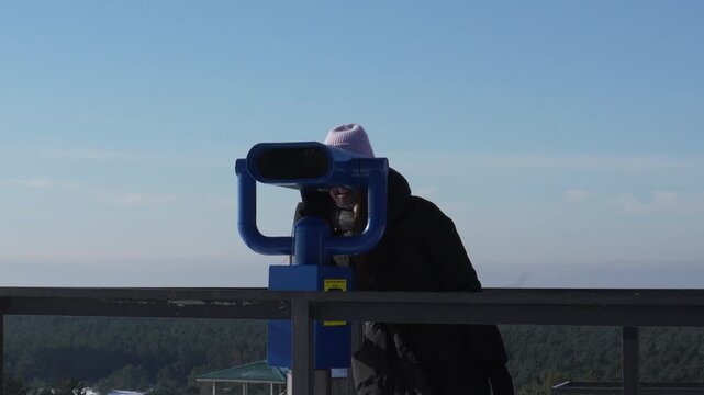 Kaliningrad landmarks. Dune Efa in winter, a popular vantage point overlooking the Baltic Sea. A woman surveys the sights through a pair of stationary binoculars.