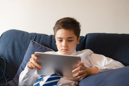 Smart schoolboy in uniform use digital tablet at home.Primary school student utilizing tablet for personalized learning,exploring educational app during after school hour,online learning,homeschooling