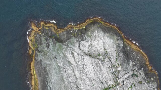 Aerial, top down view, bird view, drone flight, above husoy island. Rocky coastline with small waves Small island, some algae growing. Some seagulls flying below.