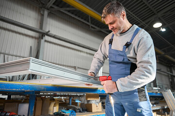 Repairman in workshop using drill to work on production of PVC windows
