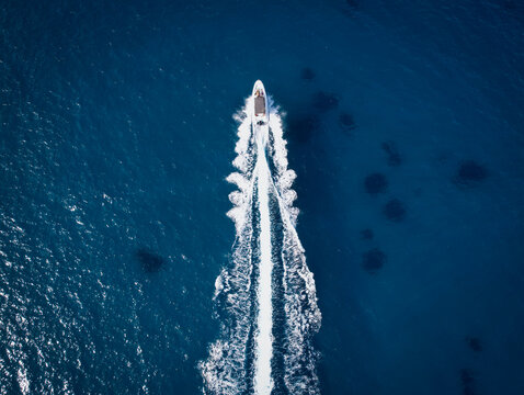 Aerial view of a white boat cutting through the deep blue sea, leaving a frothy trail in its wake, Corsica, Corsica, France.