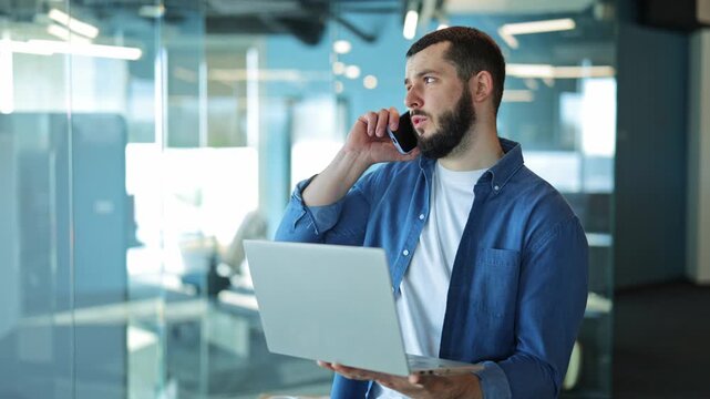 Professional person intensely focused, talking on phone, using laptop in modern office. Displays dedication, engagement, and productivity. Expresses commitment while multitasking.