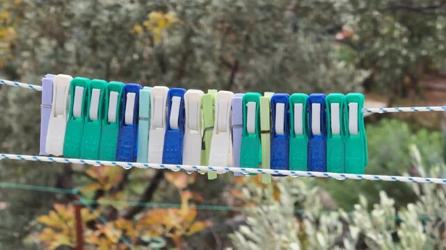 Clothespins in varying colors hanging on line outdoors with blurred foliage background
