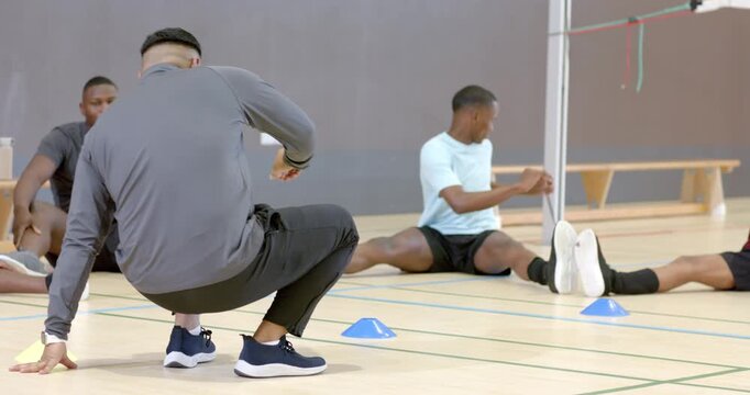 Coach in gray tracksuit arranging cones, encouraging seated players mirroring torso twists on court