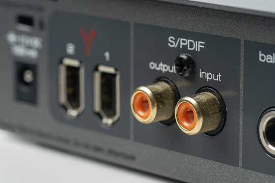 Close-up of professional audio interface rear panel featuring digital S/PDIF RCA connectors and FireWire ports for high-speed studio recording and music production connectivity on grey metal housing.
