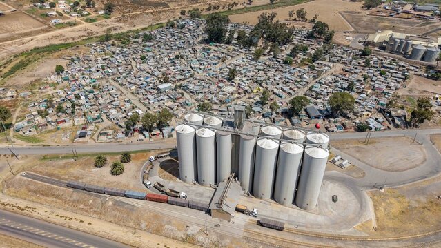 Aerial view of the stark contrast between the corrugated iron roofs of the informal settlement and the towering silos, Cape Town, Western Cape, South Africa.